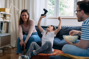 Anne ve oğlu evde video oyunu oynuyorlar. Çocuk zaferi kutluyor