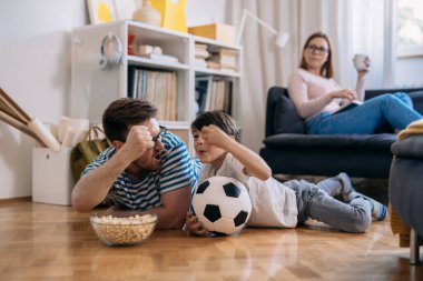 Aile evde birlikte oturma odasında futbol maçı izler. Baba ve oğul en sevdikleri takım için şerefe.