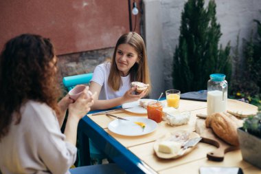 Anne ve kızı arka bahçede birlikte kahvaltı ediyorlar.