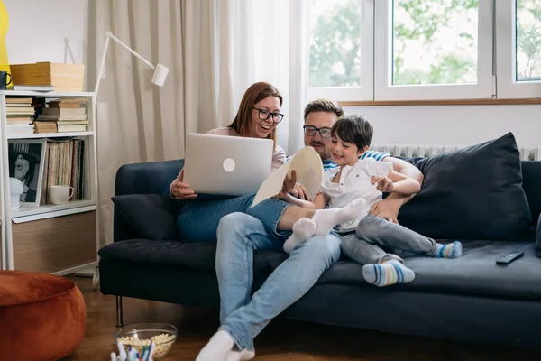 family smiling and using laptop at home. sitting on sofa in living room