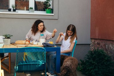 mother and daughter feeding their dog while having breakfast in backyard