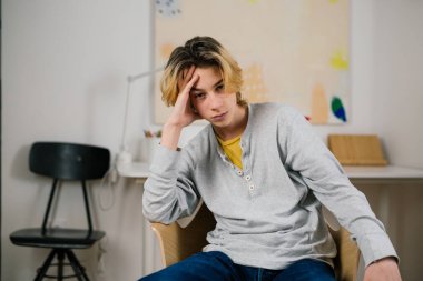 Müsait olmayan genç çocuk evde oturmuş kameraya bakıyor.