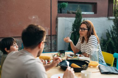 Üç kişilik aile bahçede öğle yemeği yiyor.