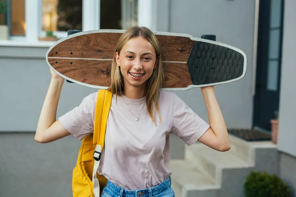 teenager girl holding surf skateboard on shoulders and looking at camera