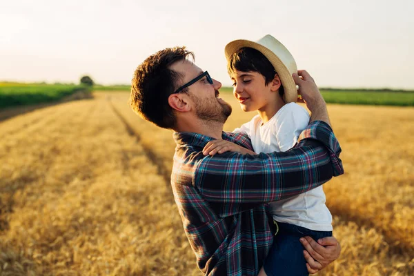 father and son enjoying time outdoor in wheat field. father holding son in arms