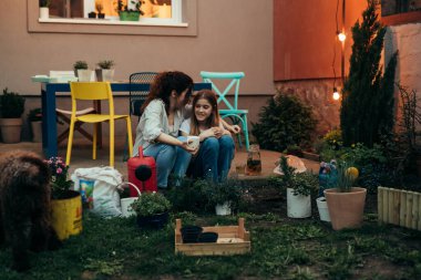 mother with her daughter sitting in backyard while gardening houseplants