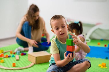 caucasian boy playing with wooden cubes toy in daycare