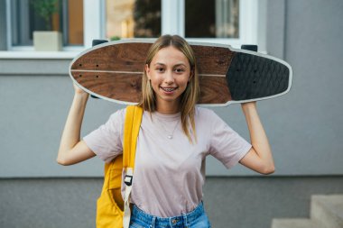 teenager with skateboard standing in front of her house