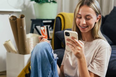 smiling teenager using smartphone for online shopping from her home