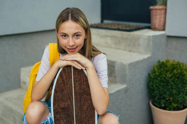 teenager with skateboard sitting on front step in front of her house