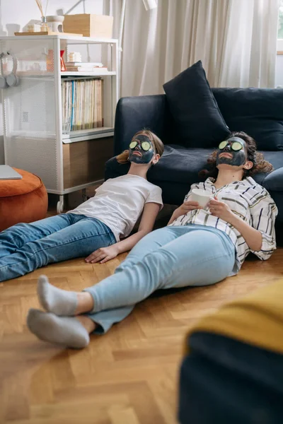 mother and daughter with cosmetic face mask relaxing in their living room