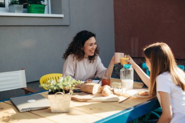 Anne ve kızı arka bahçede birlikte kahvaltı ediyorlar.