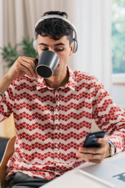 Adam kahve içiyor ve evde cep telefonu kullanıyor.
