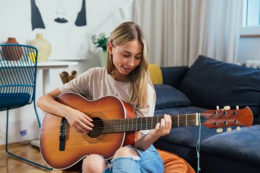 Genç bayan odasında akustik gitar çalıyor.