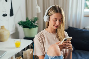 Müzik dinleyen, kulaklık takan ve akıllı telefon kullanan genç bir kız.