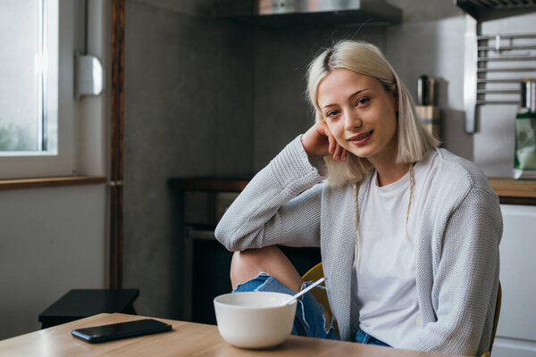 young adult generation z woman sits in her kitchen and looking at camera