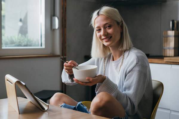 young caucasian woman eating breakfast and using digital tablet at home