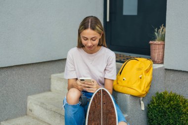 Öğrenci kız evinin önünde otururken cep telefonunu kullanıyor.