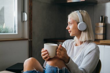 Kulaklıklı genç bir kadın sabah kahvesini yudumlarken gözlerini kaçırıyor.