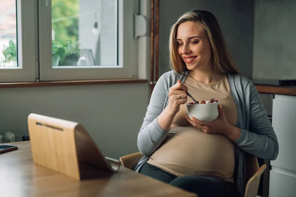 年轻的成年孕妇在家吃水果和使用数码平板电脑 — 图库照片
