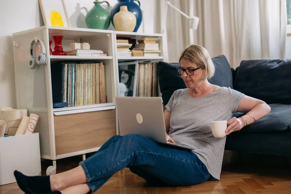中年妇女坐在客厅的地板上 使用笔记本电脑 — 图库照片