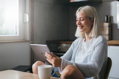 Genç bir kadın yemek masasında otururken dijital tablet kullanıyor.