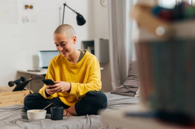 Kel kadın odasında cep telefonu kullanıyor.