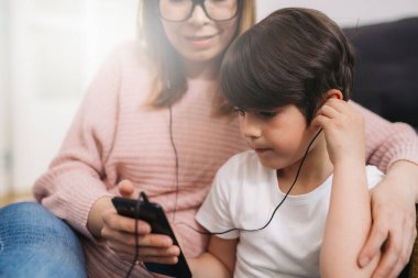 Anne ve oğul kulaklıkla müzik dinlerler.
