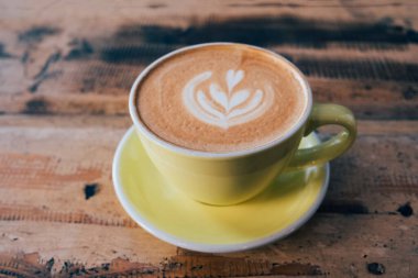 Bir fincan taze, nefis kapuçino kahve ve eski püskü ahşap arka planda yaprak şeklinde güzel latte sanatı. Uzayı kopyala Günaydın sıcak içecek..