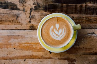 Bir fincan taze, nefis kapuçino kahve ve eski püskü ahşap arka planda yaprak şeklinde güzel latte sanatı. Üst görünüm, boşluğu kopyala. Günaydın sıcak içecek..