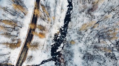 Dağ yolu, ağaçlar ve nehrin karların altındaki yüksek açılı hava manzarası. Kış manzarası, kuş bakışı manzara..