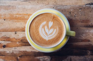 Bir fincan taze, nefis kapuçino kahve ve eski püskü ahşap arka planda yaprak şeklinde güzel latte sanatı. Üst görünüm, boşluğu kopyala. Günaydın sıcak içecek..