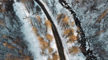 Dağ yolu, ağaçlar ve nehrin karların altındaki yüksek açılı hava manzarası. Kış manzarası, kuş bakışı manzara..