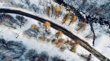 Dağ yolu, ağaçlar ve nehrin karların altındaki yüksek açılı hava manzarası. Kış manzarası, kuş bakışı manzara..