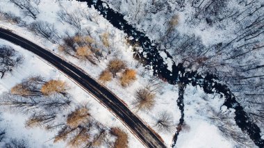 Dağ yolu, ağaçlar ve nehrin karların altındaki yüksek açılı hava manzarası. Kış manzarası, kuş bakışı manzara..