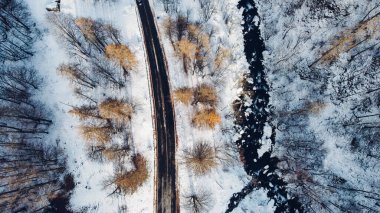 Dağ yolu, ağaçlar ve nehrin karların altındaki yüksek açılı hava manzarası. Kış manzarası, kuş bakışı manzara..