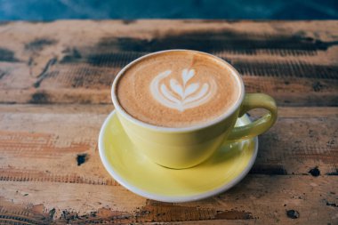 Bir fincan taze, nefis kapuçino kahve ve eski püskü ahşap arka planda yaprak şeklinde güzel latte sanatı. Uzayı kopyala Günaydın sıcak içecek..