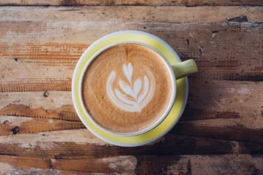 Bir fincan taze, nefis kapuçino kahve ve eski püskü ahşap arka planda yaprak şeklinde güzel latte sanatı. Üst görünüm, boşluğu kopyala. Günaydın sıcak içecek..