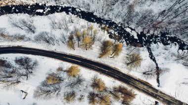 Dağ yolu, ağaçlar ve nehrin karların altındaki yüksek açılı hava manzarası. Kış manzarası, kuş bakışı manzara..