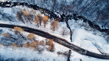 Dağ yolu, ağaçlar ve nehrin karların altındaki yüksek açılı hava manzarası. Kış manzarası, kuş bakışı manzara..