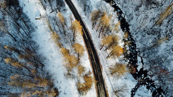 Dağ yolu, ağaçlar ve nehrin karların altındaki yüksek açılı hava manzarası. Kış manzarası, kuş bakışı manzara..