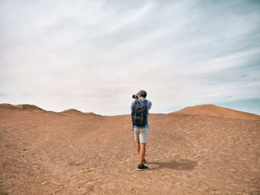 Asyalı erkek sırt çantalı manzara fotoğrafçısı tepenin arkasında fotoğraf çekiyor.