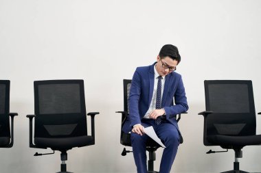 Asyalı genç erkek iş arayan, kafası aşağıda sandalyede oturan hayal kırıklığına uğramış ve mağlup olmuş görünüyor.