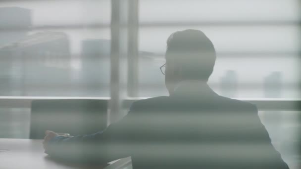 成熟したアジアの経営者が椅子から立ち上がり窓から街を眺め — ストック動画