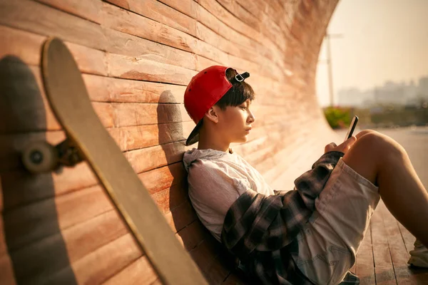 Tiener Aziatische Skateboarder Jongen Kijken Naar Mobiele Telefoon Terwijl Rusten — Stockfoto