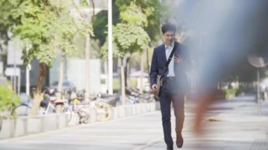 happy and successful young asian business man walking in the street in modern city
