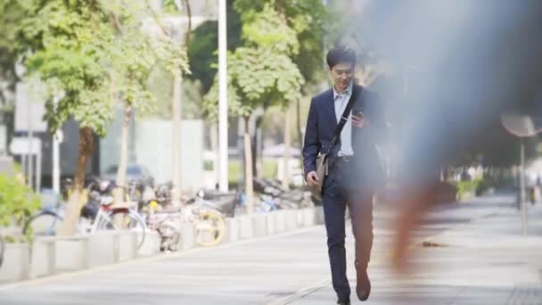 幸せで成功した若いアジア人のビジネスマンが近代都市の通りを歩き — ストック動画