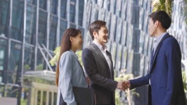 asian business associates shaking hands and talking in the street in downtown of modern city