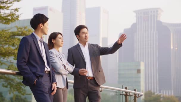 Zespół Trzech Azjatyckich Biznesmenów Stojących Świeżym Powietrzu Rozmawiających Nowoczesną Panoramą — Wideo stockowe