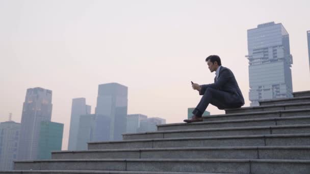 Asiático Homem Negócios Sentado Topo Dos Passos Usando Celular Pensando — Vídeo de Stock